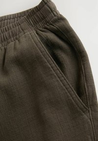 Joggers de color verde oscuro que presentan una tela texturada, cinturilla elástica y bolsillos laterales con detalles de costura visibles.
