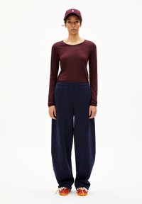 Bordeaux-rotes Langarmshirt, lockere marineblaue Jogginghose und eine burgunderfarbene Kappe mit Logo. Helle, mehrfarbige Sneaker mit Schnürsenkeln.