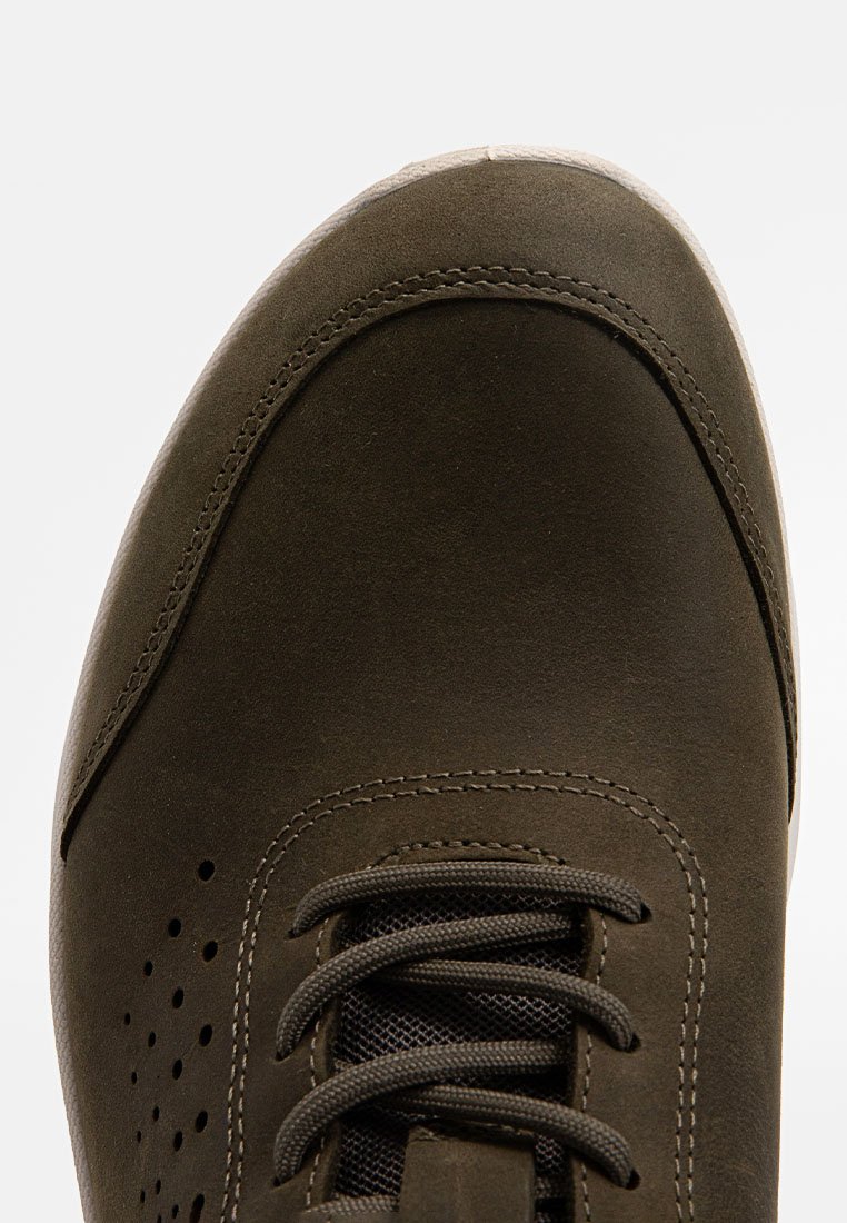 Primer plano de la parte frontal de un zapato de cuero marrón con cordones, con detalles laterales perforados y costuras cosidas.