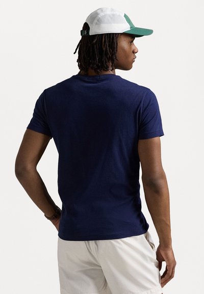 Navyblauwe t-shirt met korte mouwen van katoen, met een ronde hals. Draagt een witte en groene pet, weergegeven vanuit een achteraanzicht.