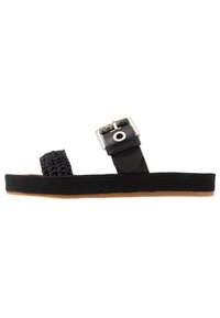Black sandal featuring a woven strap and a flat rubber sole. Metal buckle with a circular opening. Textured surface on the straps.