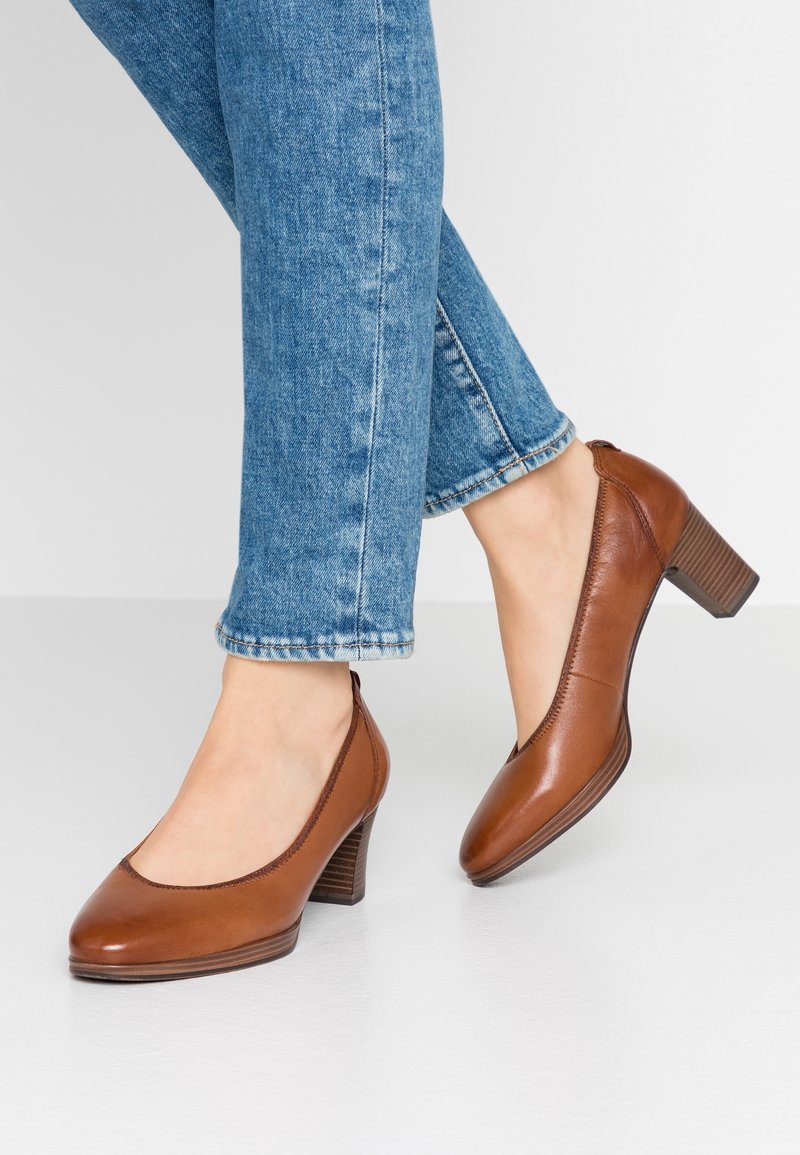 Chaussures à talons en cuir marron avec bout arrondi, petit talon et détails cousus, portées avec un jean en denim bleu à la longueur de la cheville.