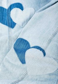 Light blue denim fabric with stitched heart-shaped patches in alternating dark and light shades of blue.