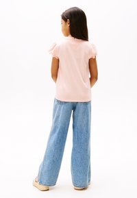 Lichtroze T-shirt met korte mouwen en gerafelde randen, gecombineerd met loszittende blauwe spijkerbroek en beige sandalen met plateauzool.