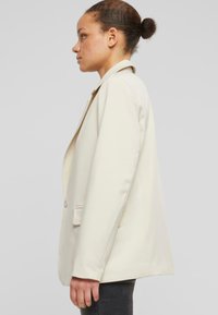 Blazer beige chiaro con vestibilità morbida, rever affilati, chiusura a un bottone e tasche laterali, realizzato in tessuto morbido.