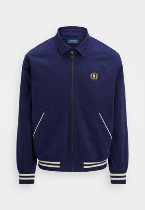 Veste de bombardier navy avec fermeture éclair, poignets côtelés et deux poches latérales. Comprend un logo brodé sur la poitrine et des accents de bandes blanches.