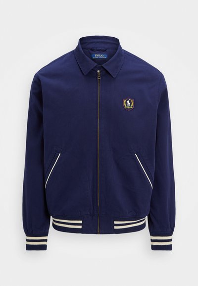 Jūras spēku bumbvedēja jaka ar rāvējslēdzēju, ribotu piedurkņu galiem un divām sānu kabatām. Satur logo uz krūšu daļas un baltas svītras akcentiem.