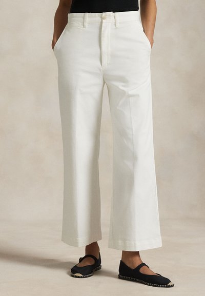 Pantalon large en coton blanc avec une taille ajustée, des poches avant et une fermeture à boutons, associé à des chaussures plates noires.