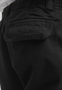Close-up of black pants showing a back pocket with a flap and detailed stitching on the fabric.