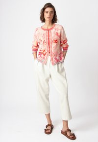 Light pink cardigan with floral embroidery, round neckline, three-quarter sleeves, paired with cream pants and brown sandals.