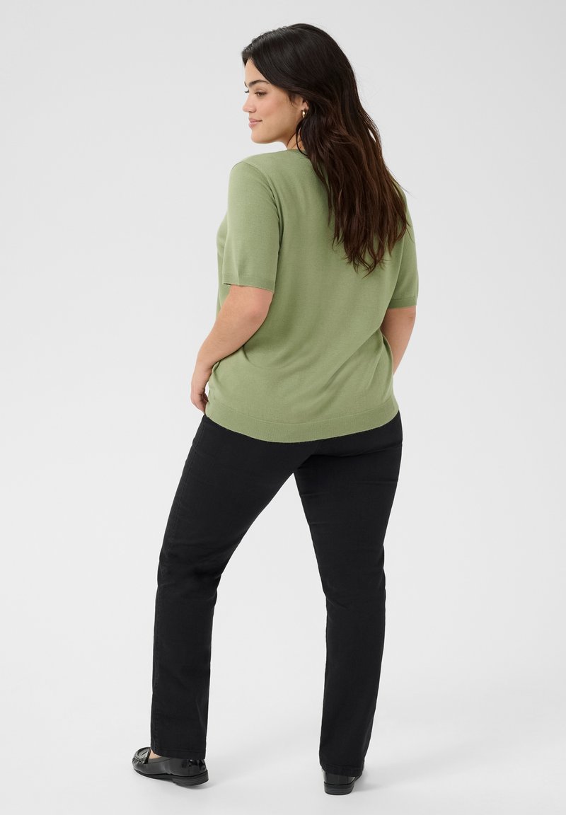 Jasnozielony t-shirt z krótkim rękawem o luźnym kroju, w połączeniu z czarnymi spodniami i czarnymi płaskimi butami. Gładka faktura i prosty design.