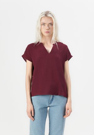 Burgunderfarget bluse med kort erme og V-hals, laget av teksturert stoff, kombinert med lyse vidde jeans i avslappet passform.