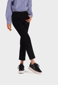 Persona che indossa jeans cropped neri a vita alta, sneakers platform nere con suola bianca e una camicia a righe blu e bianche a maniche lunghe.