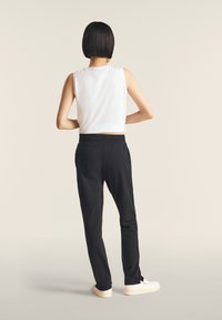 Haut sans manches blanc associé à un pantalon noir fuselé. Le pantalon possède une taille élastique. Modèle de dos, portant des baskets blanches.