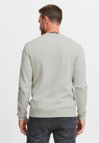 Pull en tricot gris clair avec un col rond et des poignets c�ôtelés. Présente un motif texturé et une petite touche de rayures à l'ourlet.