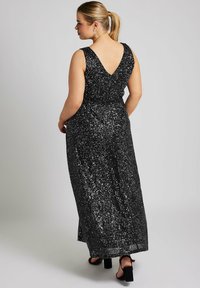 Vestido maxi negro con lentejuelas, con tirantes anchos y espalda en forma de V. Presenta una cintura ajustada y una falda fluida, complementado con sandalias negras de tacón bloque.