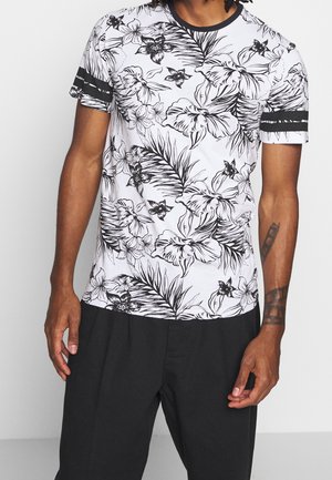 Koszulka z krótkim rękawem w kolorze białym z czarnymi kwiatowymi i liściastymi wzorami, z okrągłym dekoltem i czarnymi paskami akcentującymi na rękawach.