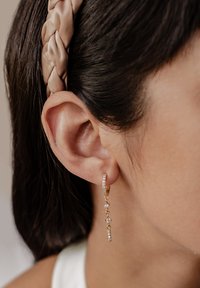 Goldene Creolen mit herabhängenden Strängen, die kleine klare Edelsteine beinhalten. Das Design umfasst schimmernde Akzente entlang der Länge.