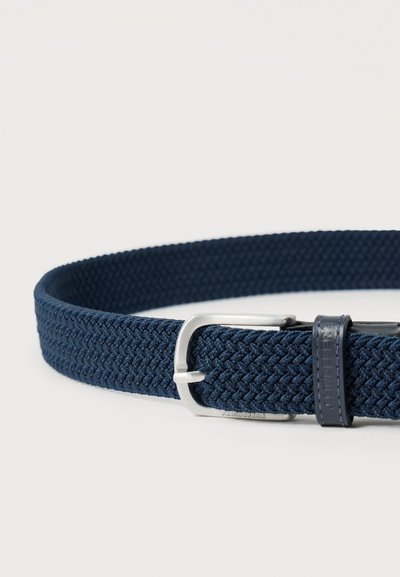 Ναυτικό μπλε πλεκτή υφασμάτινη ζώνη με ασημένια μεταλλική αγκράφα και λεπτομέρεια από δερμάτινο θηκάρι ναυτικού χρώματος σε ανοιχτό φόντο.