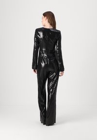 Black sequin jumpsuit with long sleeves, fitted bodice, and flared legs. Smooth texture with reflective sequins and a back zipper closure.