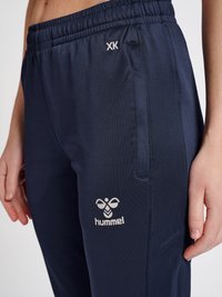 Navyblauwe sportbroek van gladde stof, met een elastische tailleband, zijzakken en een wit "hummel" logo op de bovenbeen.