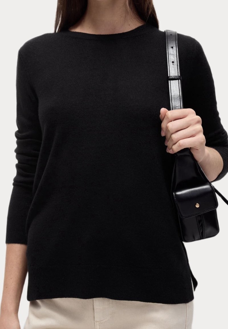 Maglione nero a maniche lunghe con scollatura a girocollo e polsini a costine; texture liscia. Borsa a tracolla nera con dettagli in hardware dorato.