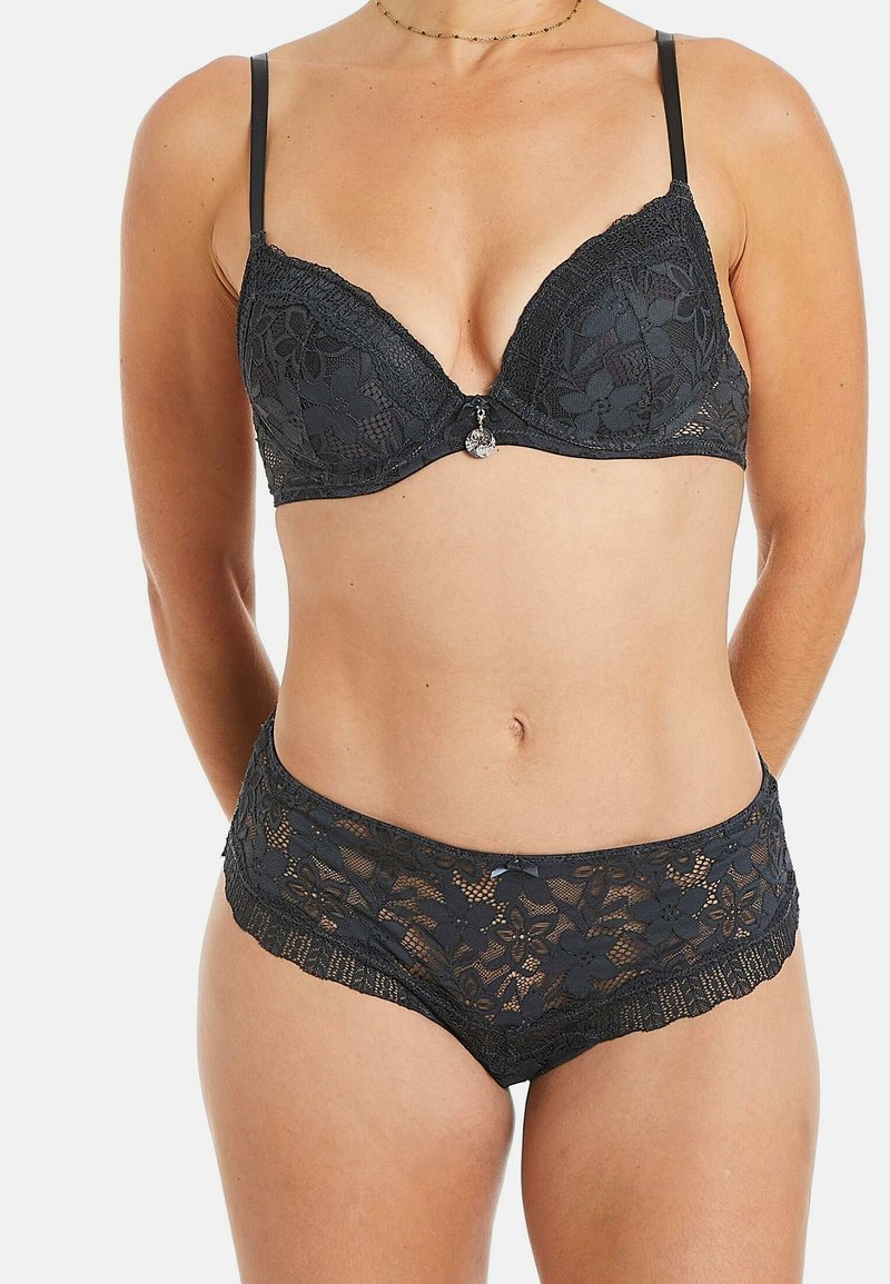 Un soutien-gorge en dentelle noire et un basique taille haute assorti présentent des motifs floraux et des bords festonnés. Bretelles ajustables et accent en métal décoratif.