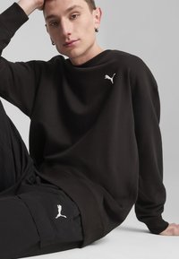 Czarna bluzka z długim rękawem z prążkowanym okrągłym dekoltem i białym logo Pumy na piersi, w zestawie z czarnymi spodniami cargo z podobnym logo.