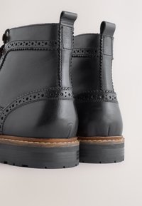 Schwarze Leder-Stiefeletten mit Brogue-Details, einer glatten Textur und einer strapazierfähigen Gummisohle mit kontrastierendem braunem Zwischensohle.