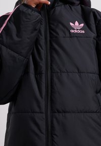 Black padded jacket with a glossy texture, featuring a front zipper, two pink accent stripes on the sleeves, and a small pink adidas logo.