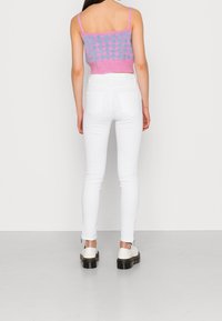 Jeans blancos ajustados con una cintura alta y un detalle de cremallera en la parte frontal. Combinados con un top corto de punto en tonos rosa y azul que presenta un diseño con patrón.
