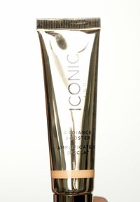 Tubo squeezabile argentato di ICONIC London Radiance Booster, con testo nero e una fascia di colore pesca nella parte inferiore. Superficie liscia e riflettente.