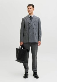 Szary wełniany dwurzędowy blezer, pasujące spodnie, czarne skórzane buty, trzymająca matową czarną torbę typu tote; pod spodem schludna koszula i krawat.