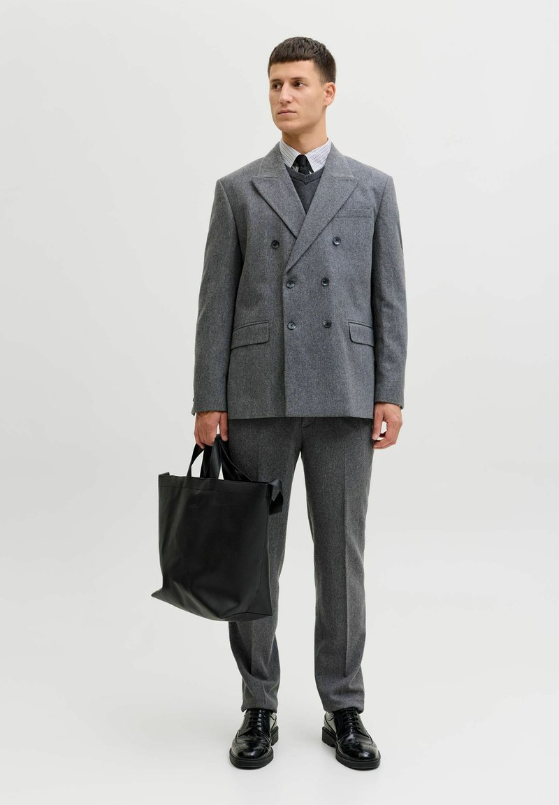 Szary wełniany dwurzędowy blezer, pasujące spodnie, czarne skórzane buty, trzymająca matową czarną torbę typu tote; pod spodem schludna koszula i krawat.
