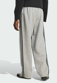 Sivé tepláky s voľným strihom, zdobené čiernymi vertikálnymi pruhmi po stranách a elastickým pásom; vyrobené z mäkkej tkaniny.