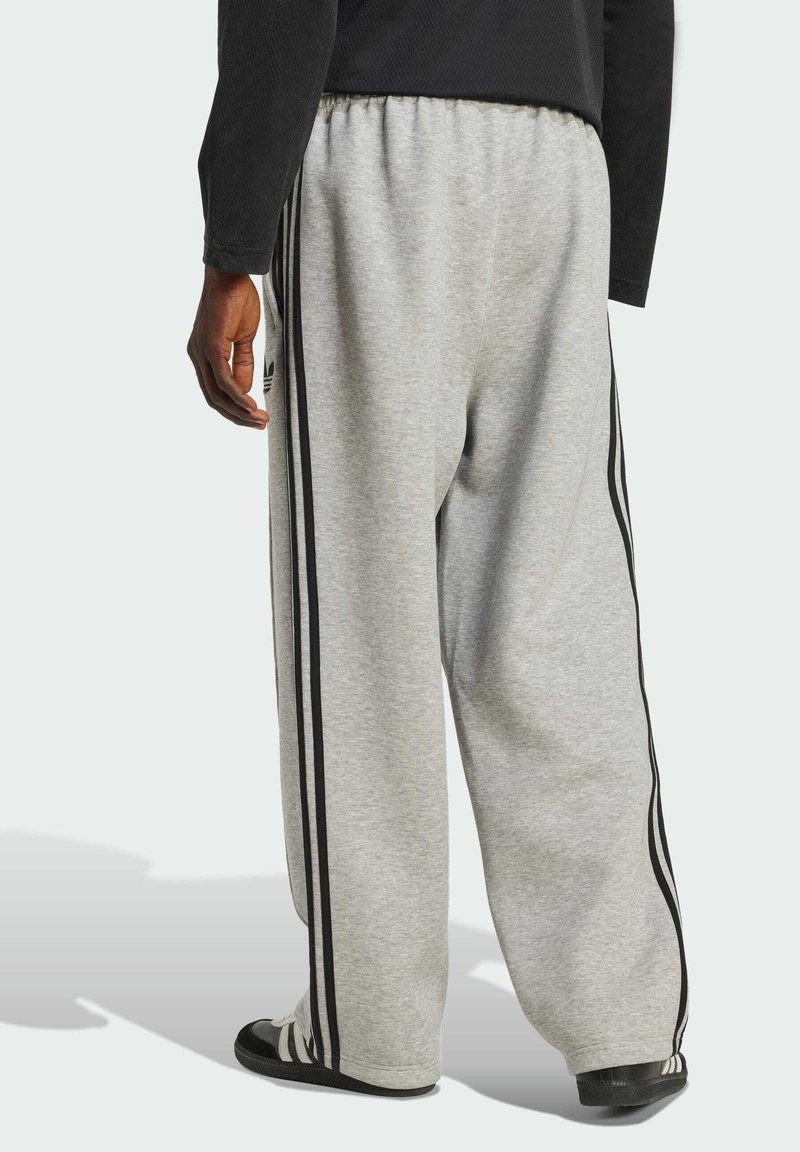 Pantalones deportivos grises con un corte relajado, que presentan franjas verticales negras a lo largo de los lados y una cinturilla elástica; fabricados en una tela suave.