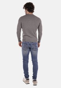 Pullover grigio a maniche lunghe con design aderente, indossato con jeans blu. I jeans hanno una finitura sbiadita e tasche posteriori con dettagli di cucitura.