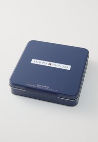 Blå metaldåse med Tommy Hilfiger-logo. Indeholder fire par herresokker, mærket med størrelsesspecifikationer på siden.