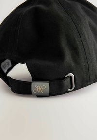 Sort baseball cap med et struktureret stof, udstyret med en justerbar metalrem og et metallisk mærke med et guld-logo bagpå.