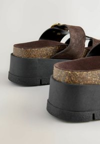 Sandale platform din brun cu talpă intermediară din plută, talpă exterioară din cauciuc negru și bretele din suede moale. Include o cataramă pentru o ajustare optimă.