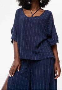 Tunique à rayures bleu marine avec une coupe décontractée, des manches courtes et un col en V. Elle présente un détail décoratif avec un lien et une texture douce.