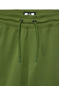 Grønne joggebukser med en glatt tekstur, med en svart og hvit etikett, elastisk midjebånd og justerbare snorer i matchende farge.