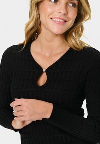 Black knitted top featuring a textured pattern, round neckline with a keyhole cutout, and a pearl accent. Long sleeves with ribbed cuffs.