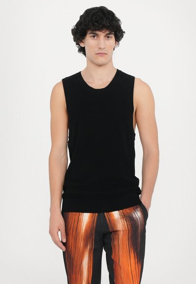 Schwarzes ärmelloses Stricktop mit Rundhalsausschnitt, figurbetontem Design und glatter Textur, kombiniert mit mehrfarbigen Druckhosen, die orangefarbene und schwarze Muster aufweisen.