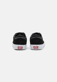 Svarte semskede sneakers med hvite gummisåler, med design som er sydd, hæltabber og røde "Vans Off the Wall" logo detaljer. Limited edition nummer.