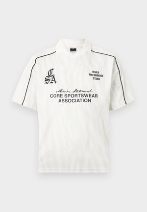 Bela športna polo majica s kratkimi rokavi s črnimi obrobami na ramenih, nežnim vzorcem zebre in črnimi logotipi s tekstom "Core Sportswear Association" in "World Performance Studio".
