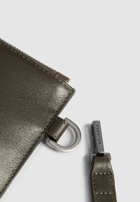 Olijfgroene leren pouch met een gladde textuur. Voorzien van een metalen rits, leren ritstrekker en een zilverkleurig metalen accent.