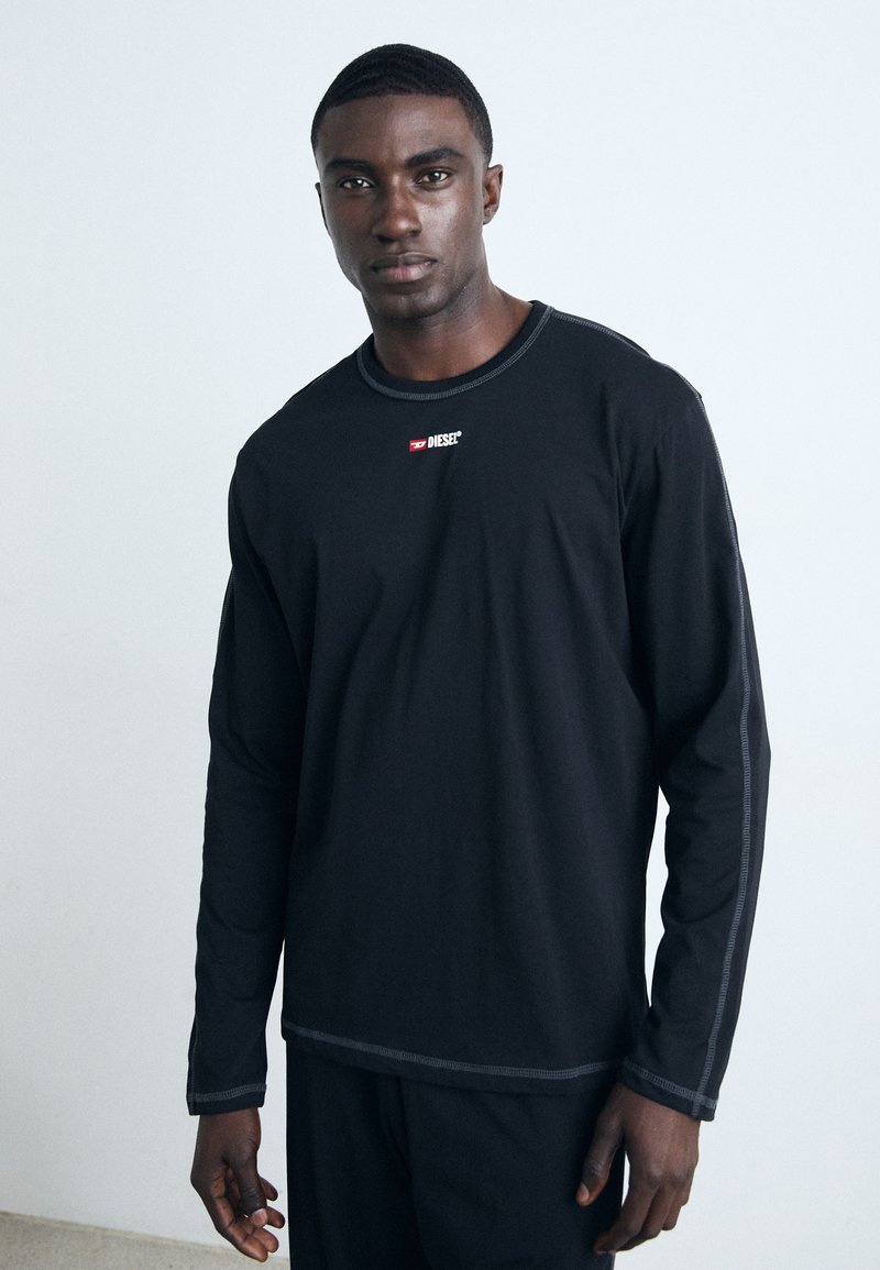 Long-sleeve black shirt made of soft fabric. Features a round neckline, contrasting gray stitching, and a red logo on the chest.