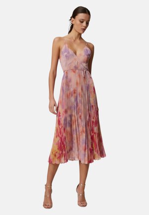 Donna che indossa un vestito midi plissettato senza maniche con un motivo floreale ad acquerello in tonalità rosa, viola e arancione, abbinato a tacchi con cinturini.