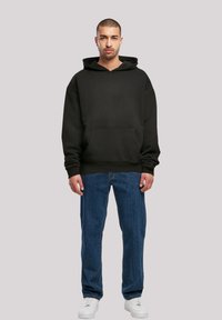 Black hooded sweatshirt with a front pocket, worn with blue jeans and white sneakers. Material appears soft, with a loose fit design.